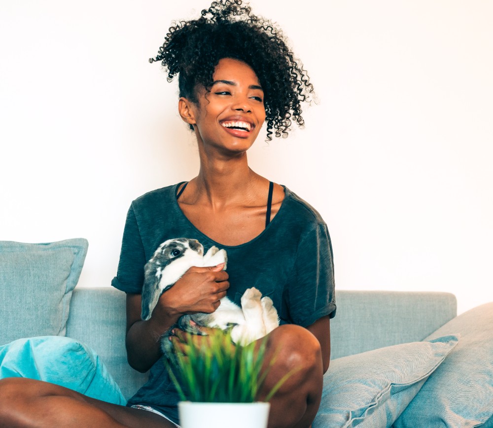 Young black woman sitting on her couch holding a bunny.