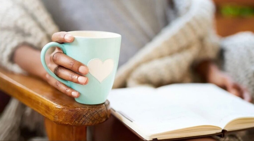 Woman's hand holding a coffee cup next to reading her journal.